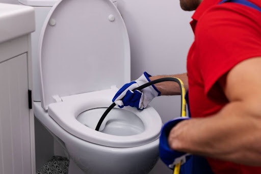 A plumber using hydro jetting equipment on a toilet.