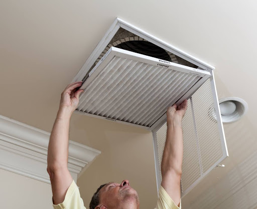 A man replacing the air filter for a central AC system.